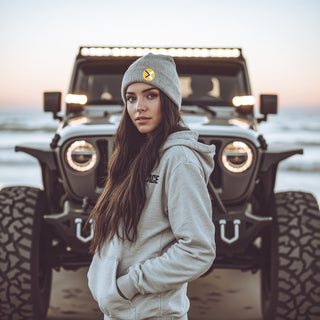 Woman on the beach standing in front of her Jeep Wrangler wearing a light grey beanie and a light grey hoodie. ottnp.com